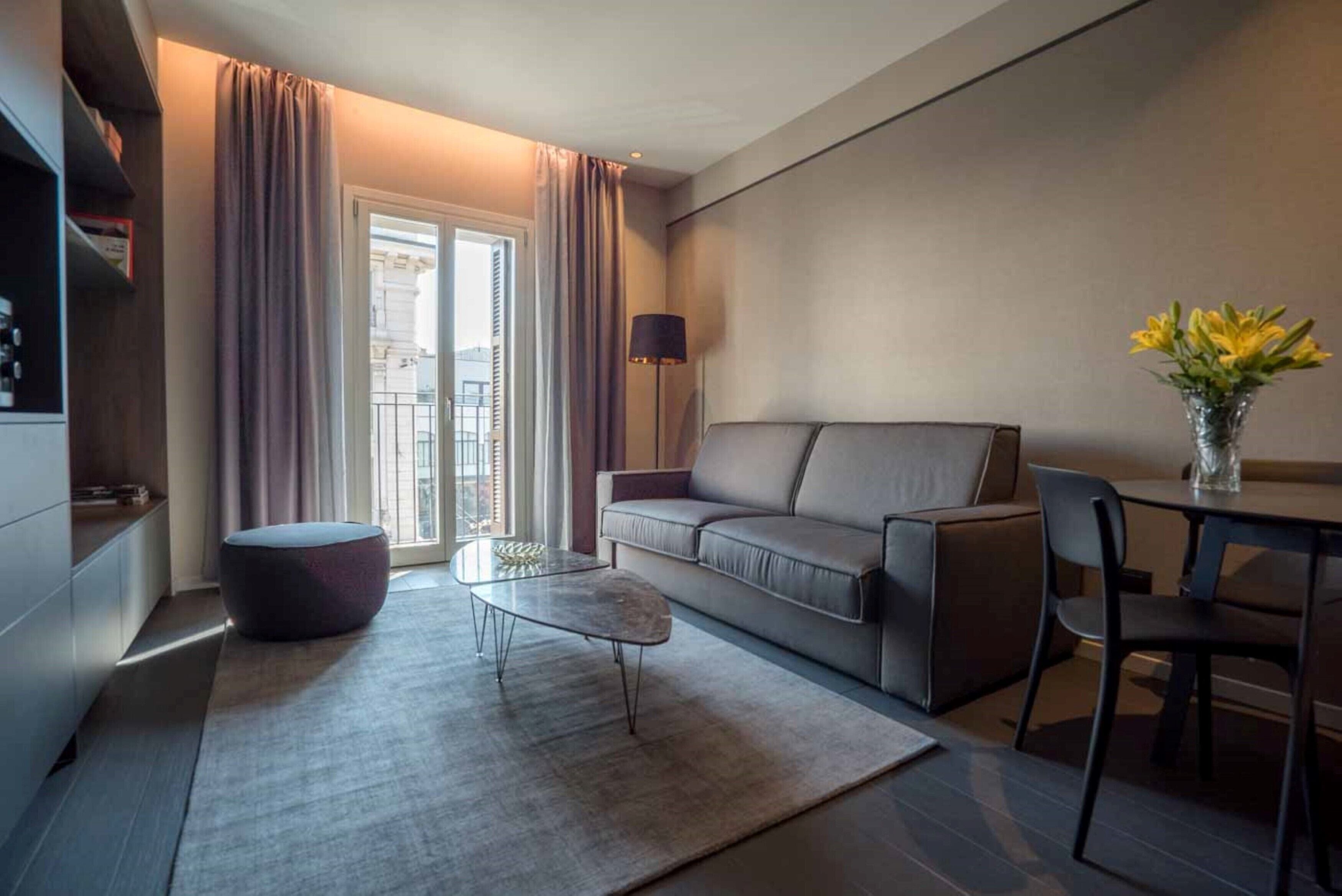 A modern living room with a sofa, ottoman, coffee table, and a dining area with chairs.