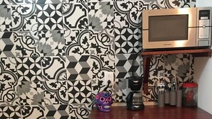 Una cocina con baldosas estampadas, microondas, cafetera y un mueble con vajilla.