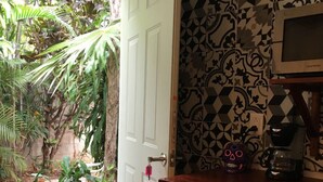 Una cocina con salpicadero de azulejos, una cafetera y una estantería con vajilla.