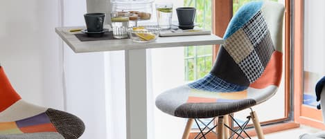 Un'area pranzo con un tavolo apparecchiato per due, una sedia con schienale patchwork e un vaso con fiori blu.