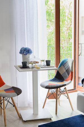 A dining area with a table set for two, a chair with a patchwork backrest, and a vase with blue flowers. - Les Suites des Tout le Monde (Sorrento)