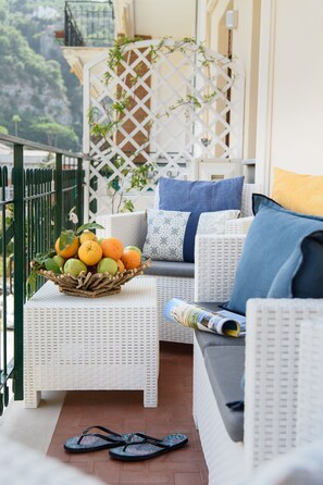 A balcony with wicker furniture, a fruit basket, and a pair of flip-flops on the floor. - Les Suites des Tout le Monde (Sorrento)