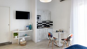 A compact living space with a kitchenette, a flat-screen TV, a dining area with two chairs, and a large window with curtains. - Les Suites des Tout le Monde (Sorrento)