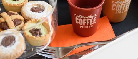 A tray with pastries, a glass of milk, and two coffee cups on a table.