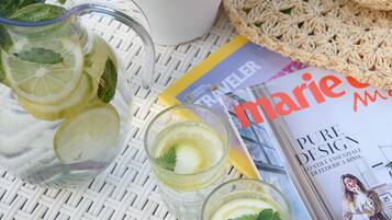 A table with a potted mint plant, a crocheted hat, a magazine, and two glasses of a lemon and mint beverage.