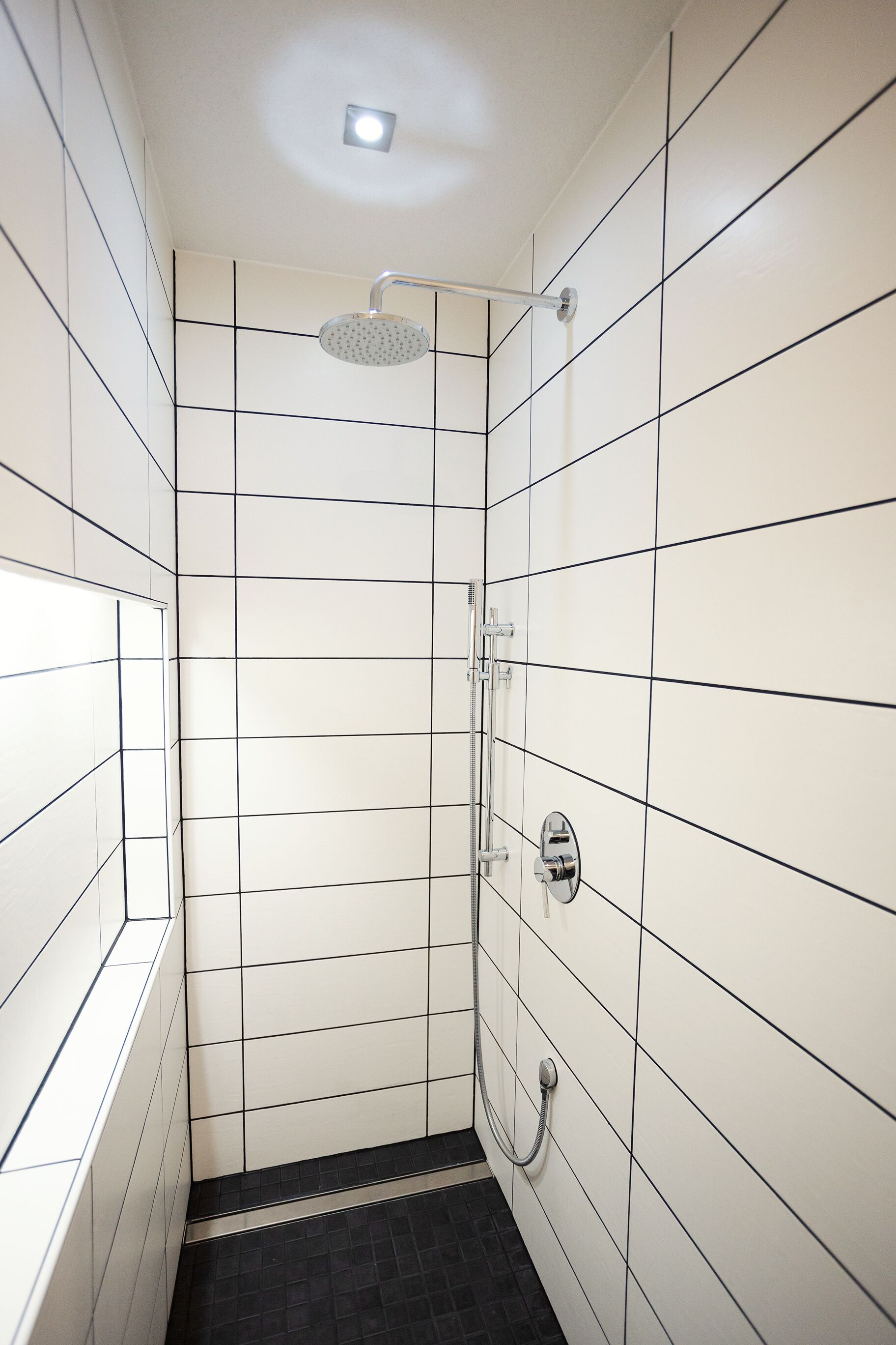 Un petit espace douche aux murs recouverts de carreaux blancs et au sol carrelé de noir.