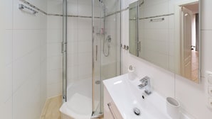Un baño moderno con ducha de vidrio, lavamanos blanco con espejo y un inodoro.