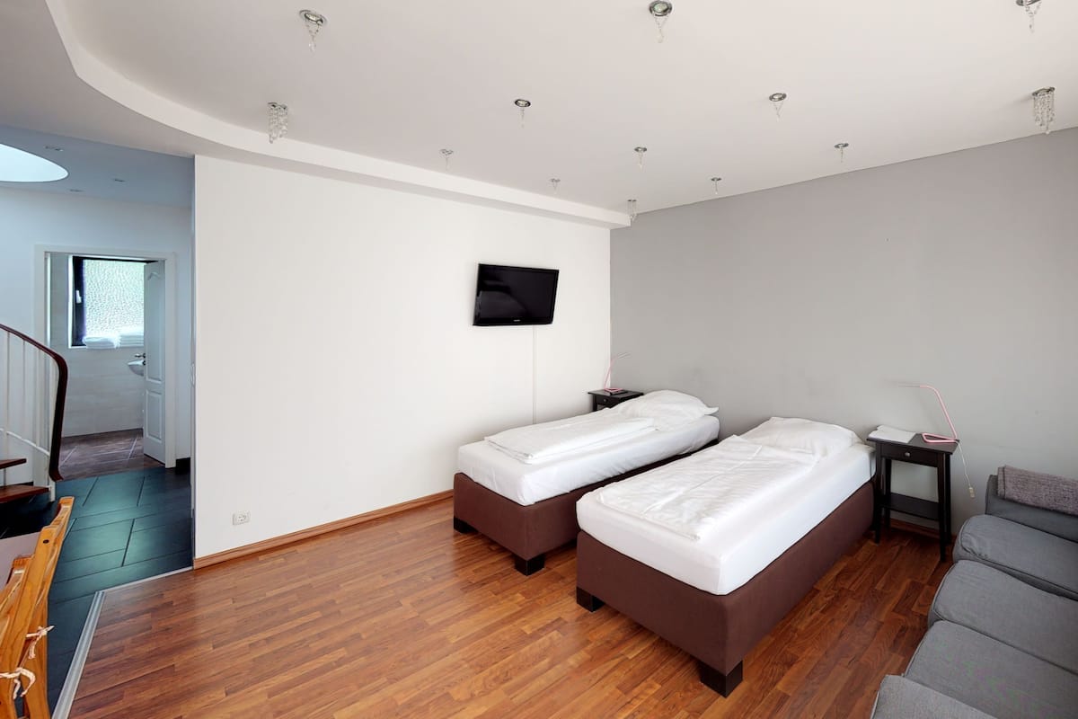 A hotel room with two single beds, a sofa, a TV, and a small bedside table.