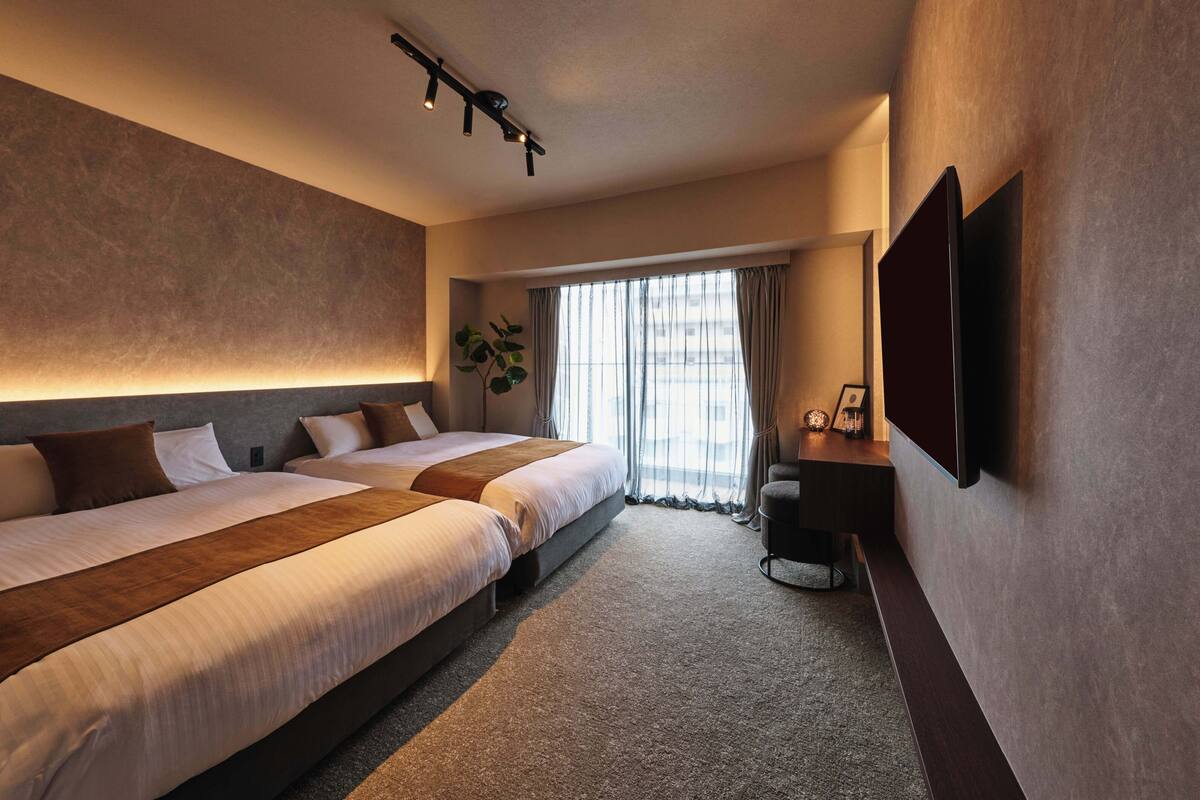 Une chambre d’hôtel avec deux lits, un téléviseur à écran plat, une plante et une fenêtre avec des rideaux.