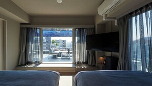A hotel room with two beds, a TV, a balcony with a sofa and table, and a city view. - Residence Hotel Hakata 20 (Fukuoka)