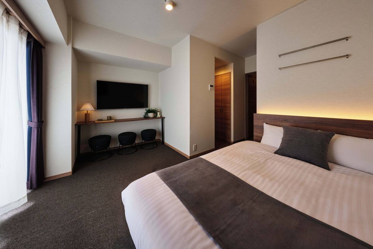 Une chambre d’hôtel avec un grand lit, un bureau avec deux chaises, un téléviseur à écran plat et une armoire en bois.