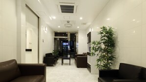 A modern hotel lobby with a reception desk, seating area, and a large potted plant. - Residence Hotel Hakata 20 (Fukuoka)