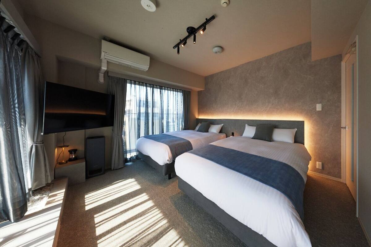 Une chambre d’hôtel avec deux lits, un téléviseur à écran plat, un appareil de climatisation et un luminaire fixé au plafond.