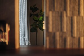 A plant in a doorway with a wooden wall and a window with curtains. - Residence Hotel Hakata 20 (Fukuoka)