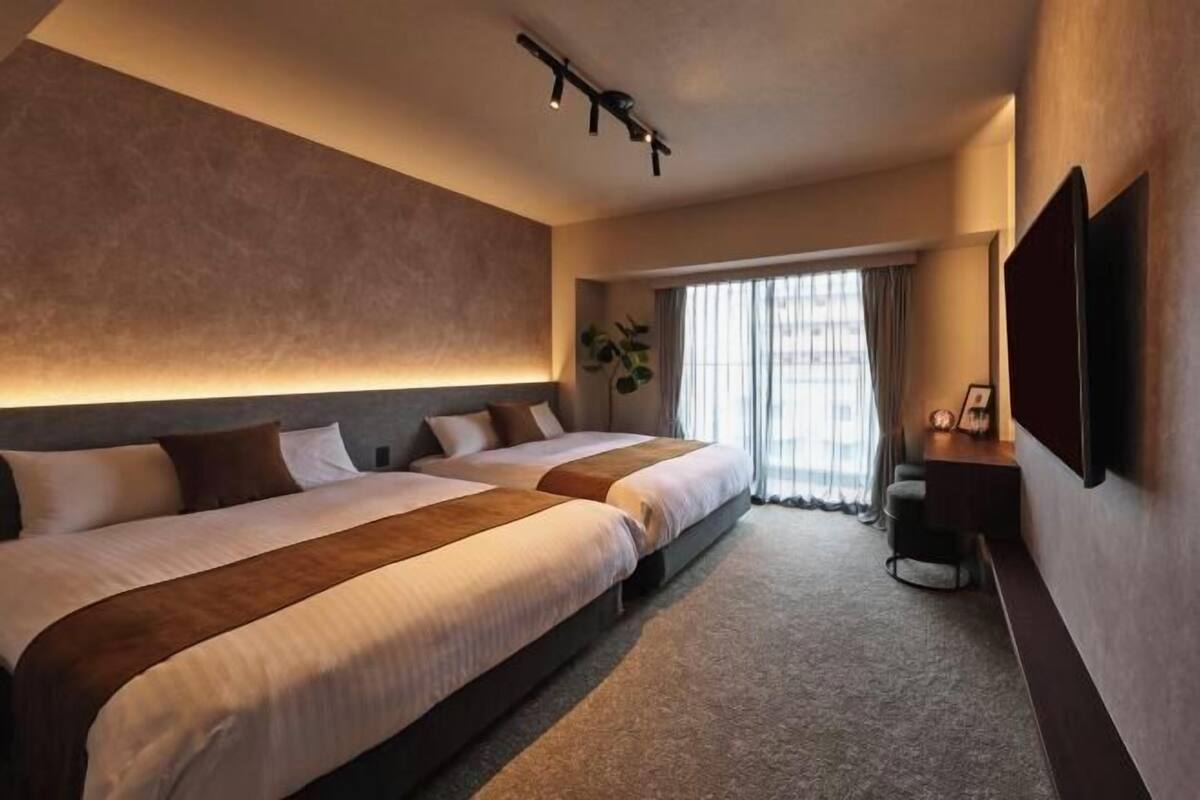 Une chambre d’hôtel avec deux lits, une télévision, un bureau et une fenêtre avec des rideaux.