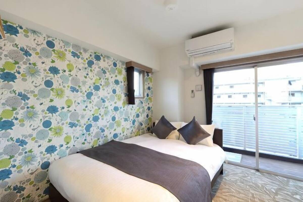 Une chambre avec un grand lit, une fenêtre donnant sur un beau paysage et un mur décoré d’un motif.