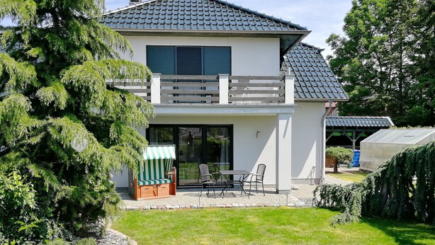 A two-story house with a balcony, a covered patio, and a greenhouse.
