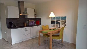 A modern kitchen with white cabinets, a coffee maker, and a dining area with a table and chairs.