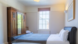 A neatly arranged bedroom with a large bed, a window with blinds, a radiator, and a wooden wardrobe. - Luxury Apartments - Churchside (Cheltenham)