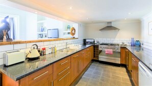 A modern kitchen with wooden cabinets, a granite countertop, a stove, and a sink. - Luxury Apartments - Churchside (Cheltenham)