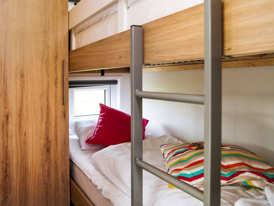 A bunk bed room with a wooden wardrobe and a window.