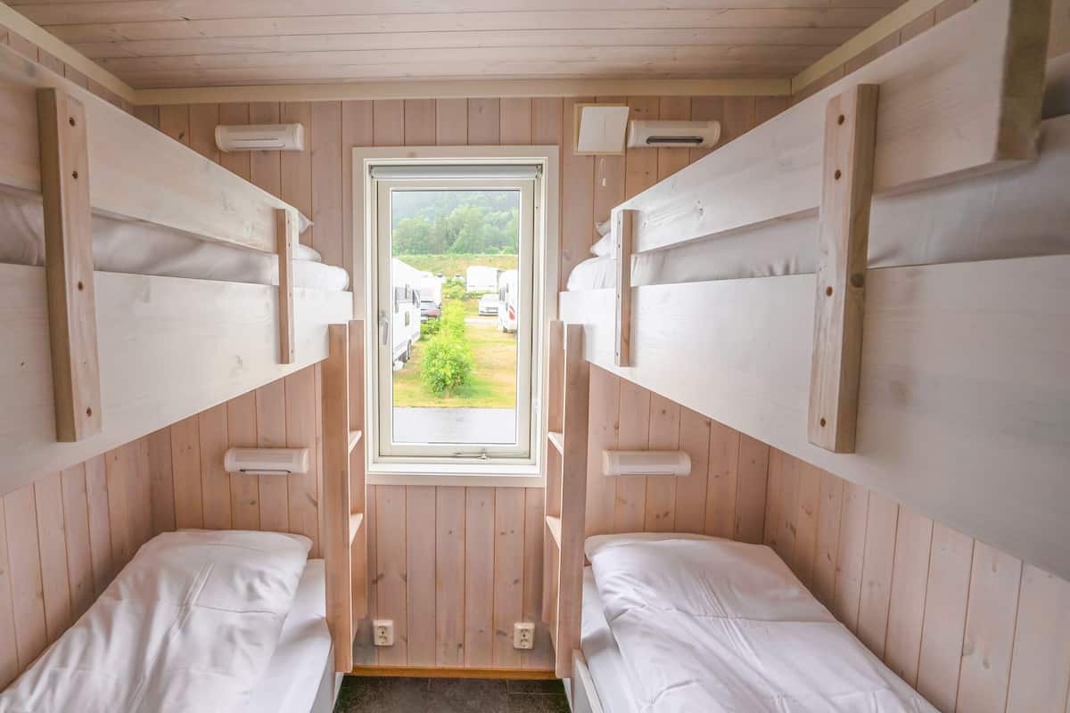 Uma cabana com duas beliches, uma janela com vista para uma paisagem verde e interior de madeira.