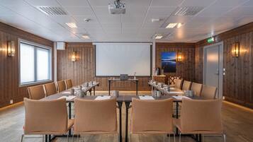 Una sala de conferències amb una taula gran, cadires, un projector, una pantalla i una paret de fusta.