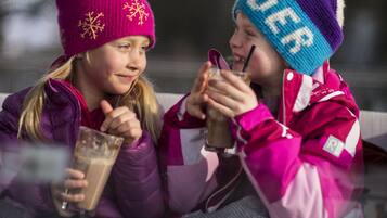 Dos personas sentadas en un trineo, con gorros y abrigos de invierno, sosteniendo bebidas.