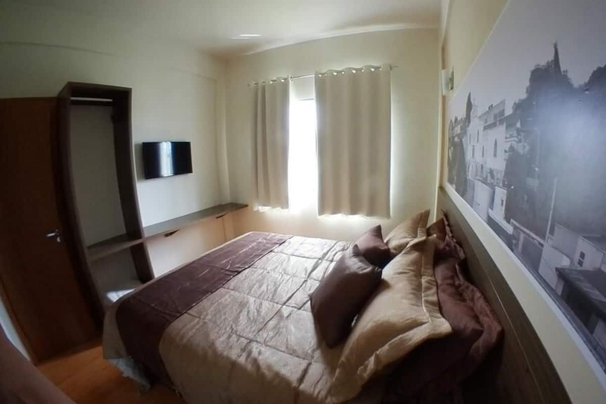 A bedroom with a bed, curtains, a mounted TV, and a cityscape poster on the wall.