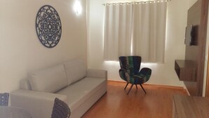 Una sala de estar con un sofá, un adorno mural estampado, una silla y una ventana con cortinas.