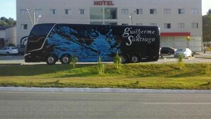 Un hotel con un cartel que dice "PIT STOP HOTEL" y un autobús con la marca "Guilherme & Santiago" estacionado frente a él.