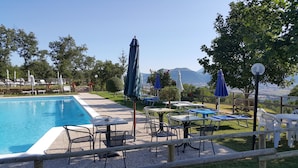 Un espace piscine agrémenté de chaises longues et de tables, entouré d’arbres et offrant une vue sur les montagnes.
