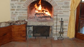 Une cheminée en pierre avec une horloge au-dessus, un banc en bois et un feu qui crépite à l’intérieur.