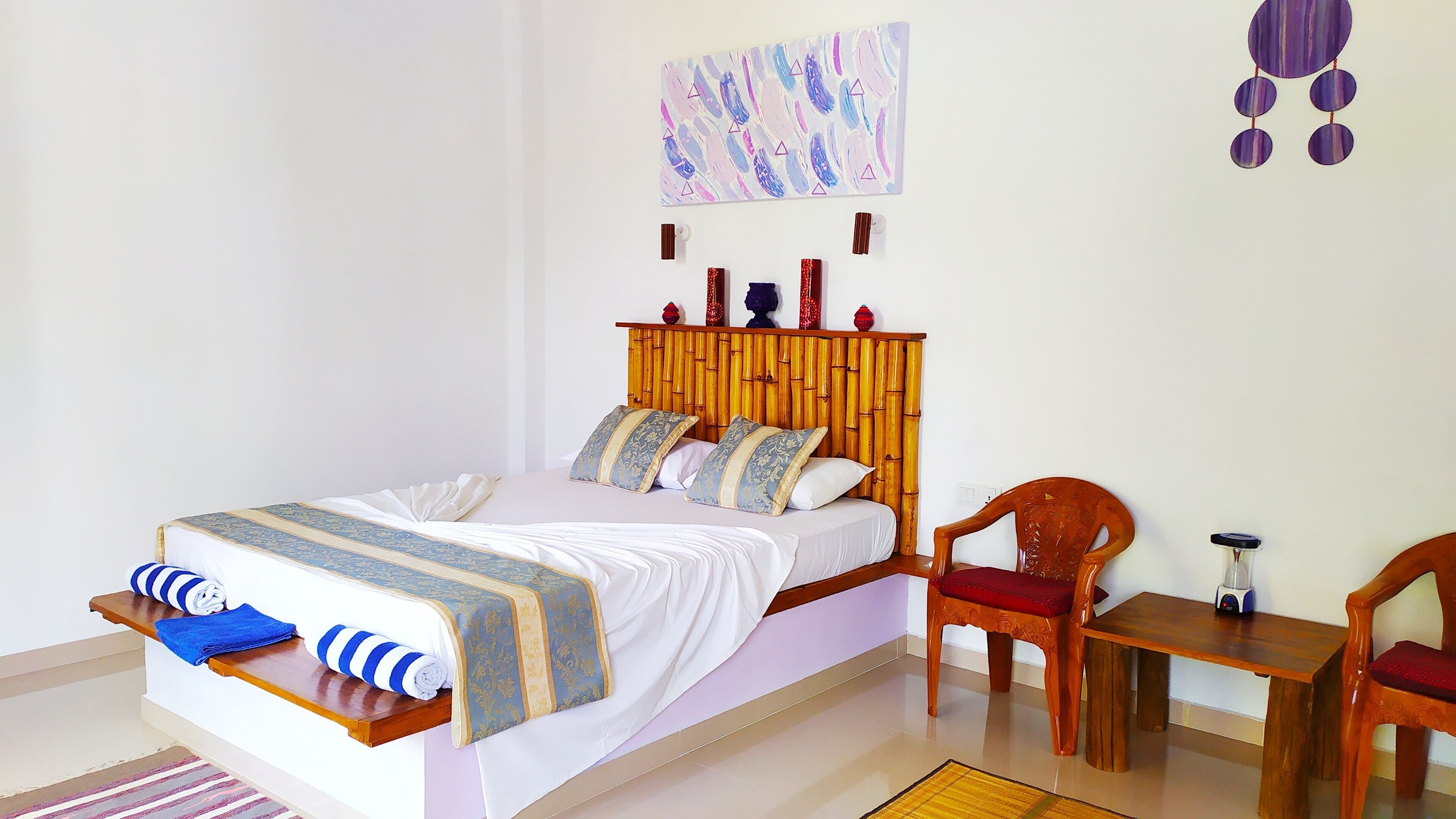 A neatly made bed with a striped blanket, a wooden headboard, and two pillows. There is a wooden chair and a small table with a radio beside the bed.