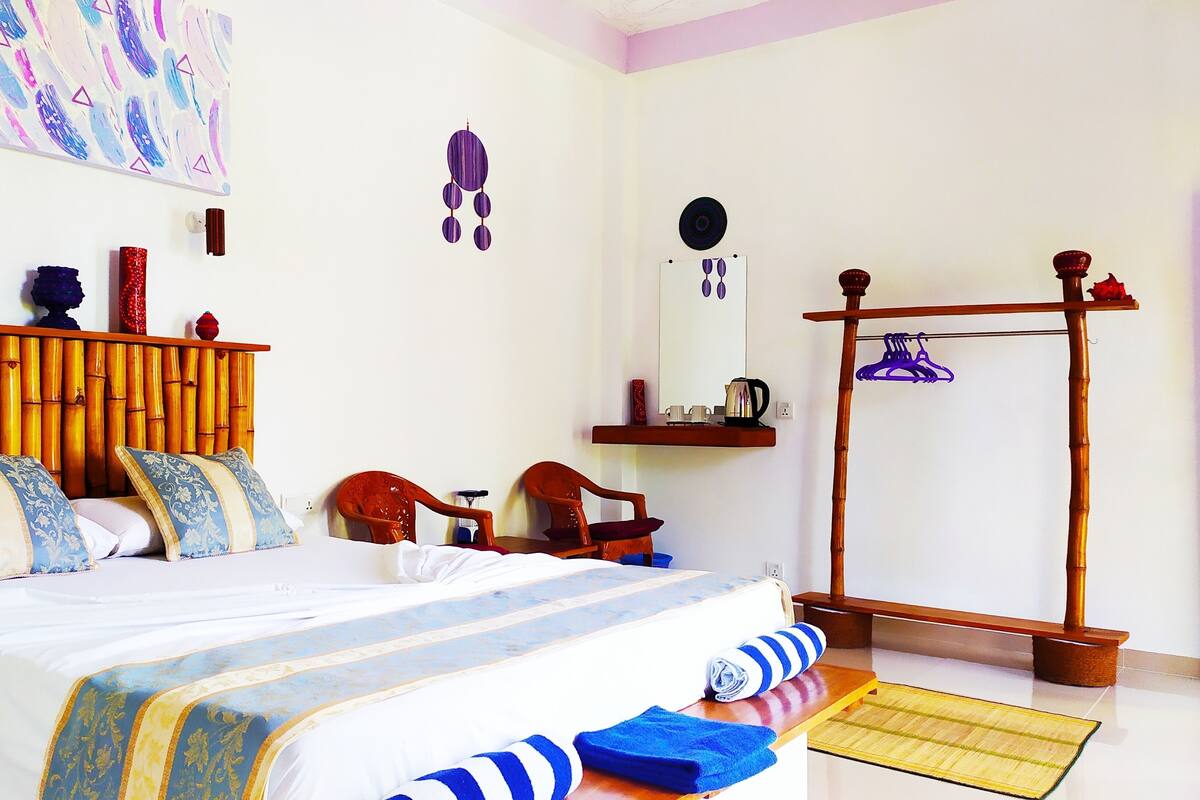 A neatly arranged bedroom with a bed, a wooden headboard, a bedside table, a chair, a hanging rack, and a wardrobe.