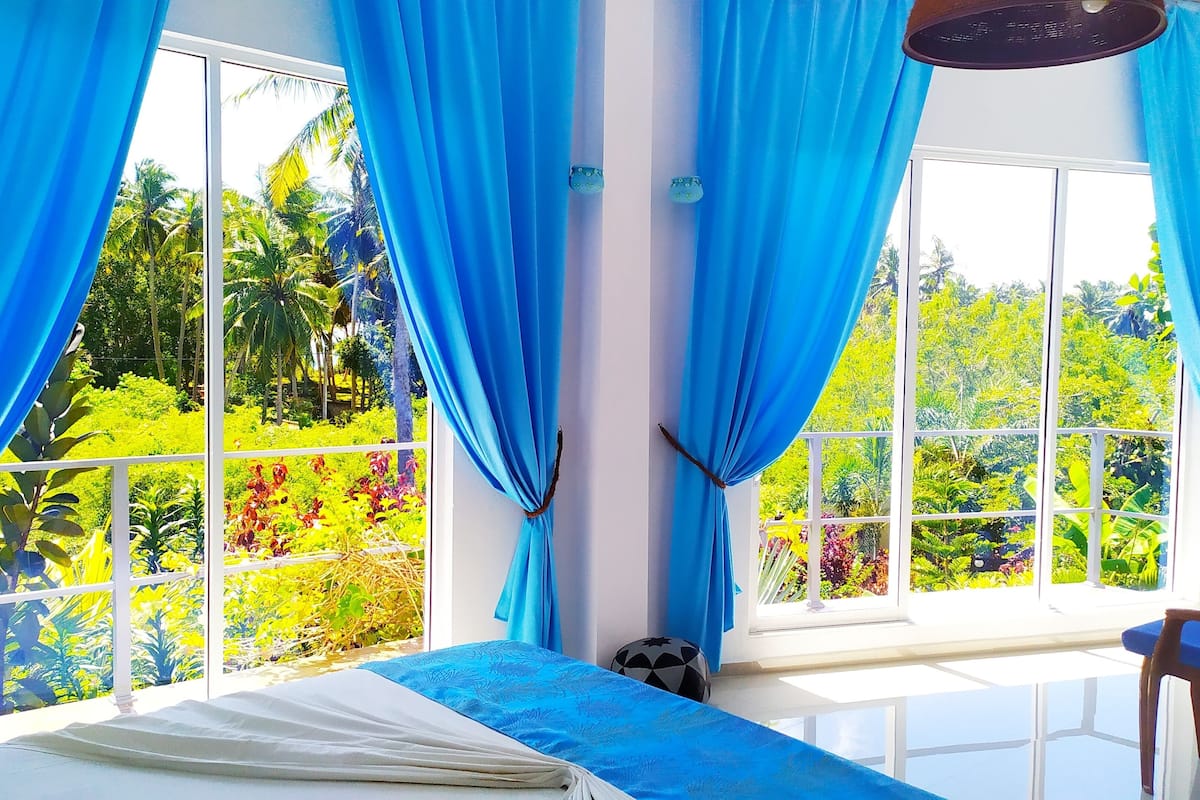 A room with a bed, a chair, and large windows with blue curtains.