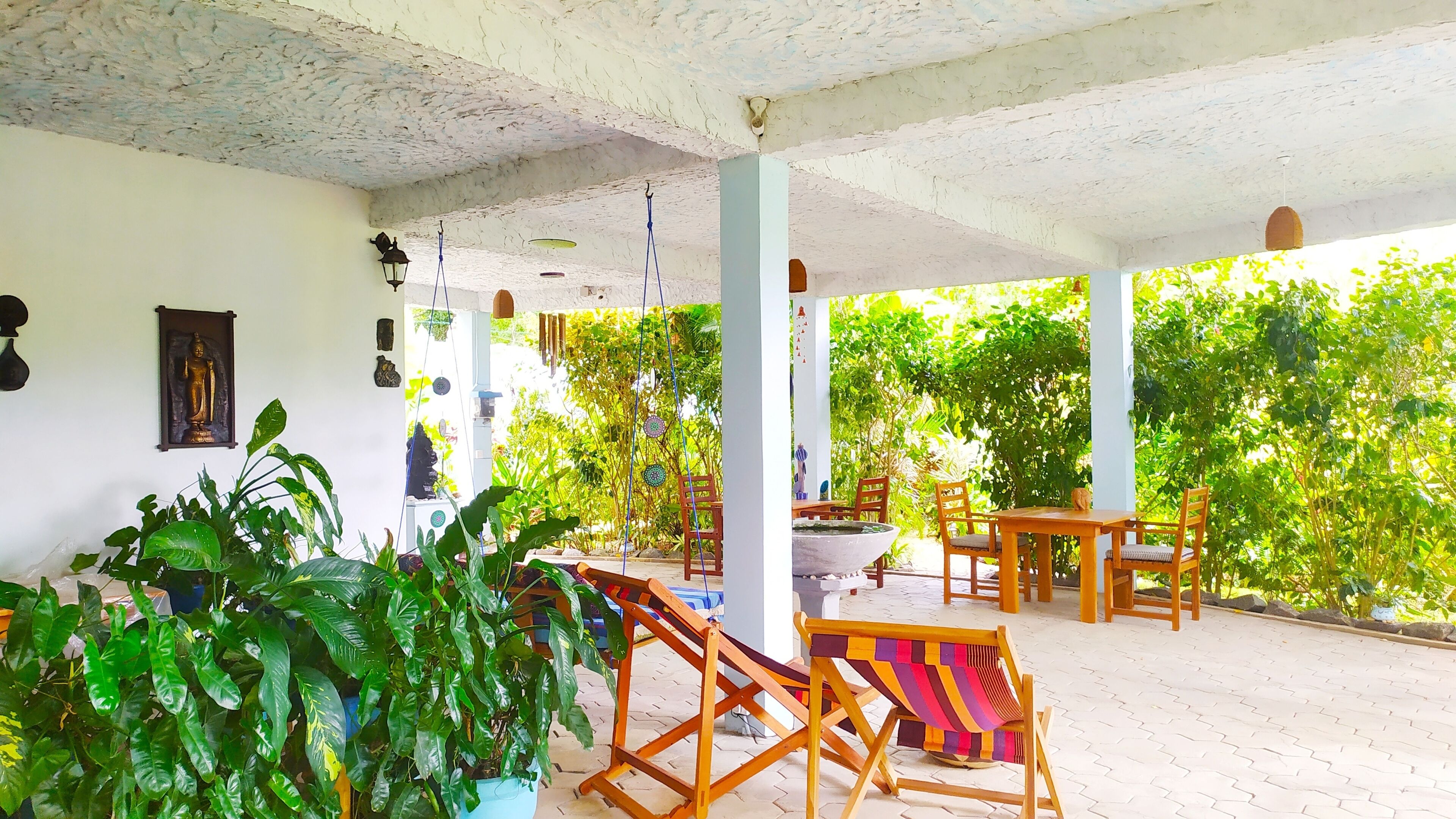 Un espacio al aire libre cubierto con muebles de madera, plantas en macetas y una estatua de Buda en la pared.