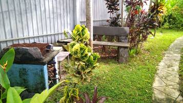 Un jardín con un banco, un cubo de basura y diversas plantas.