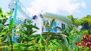 A modern building with a white facade and blue accents, surrounded by lush tropical vegetation. - Villa Modara (Kahandamodara)