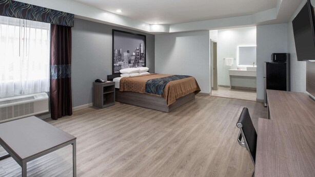 A hotel room with a bed, bedside table, desk, and a TV. - Super 8 by Wyndham Humble/Fallcreek/Houston (Humble)