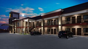 A multi-story hotel with a brick facade, multiple balconies, and a parking lot with two cars. - Super 8 by Wyndham Humble/Fallcreek/Houston (Humble)