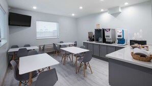 A modern kitchen with white countertops, grey chairs, and a flat-screen TV mounted on the wall. - Super 8 by Wyndham Humble/Fallcreek/Houston (Humble)
