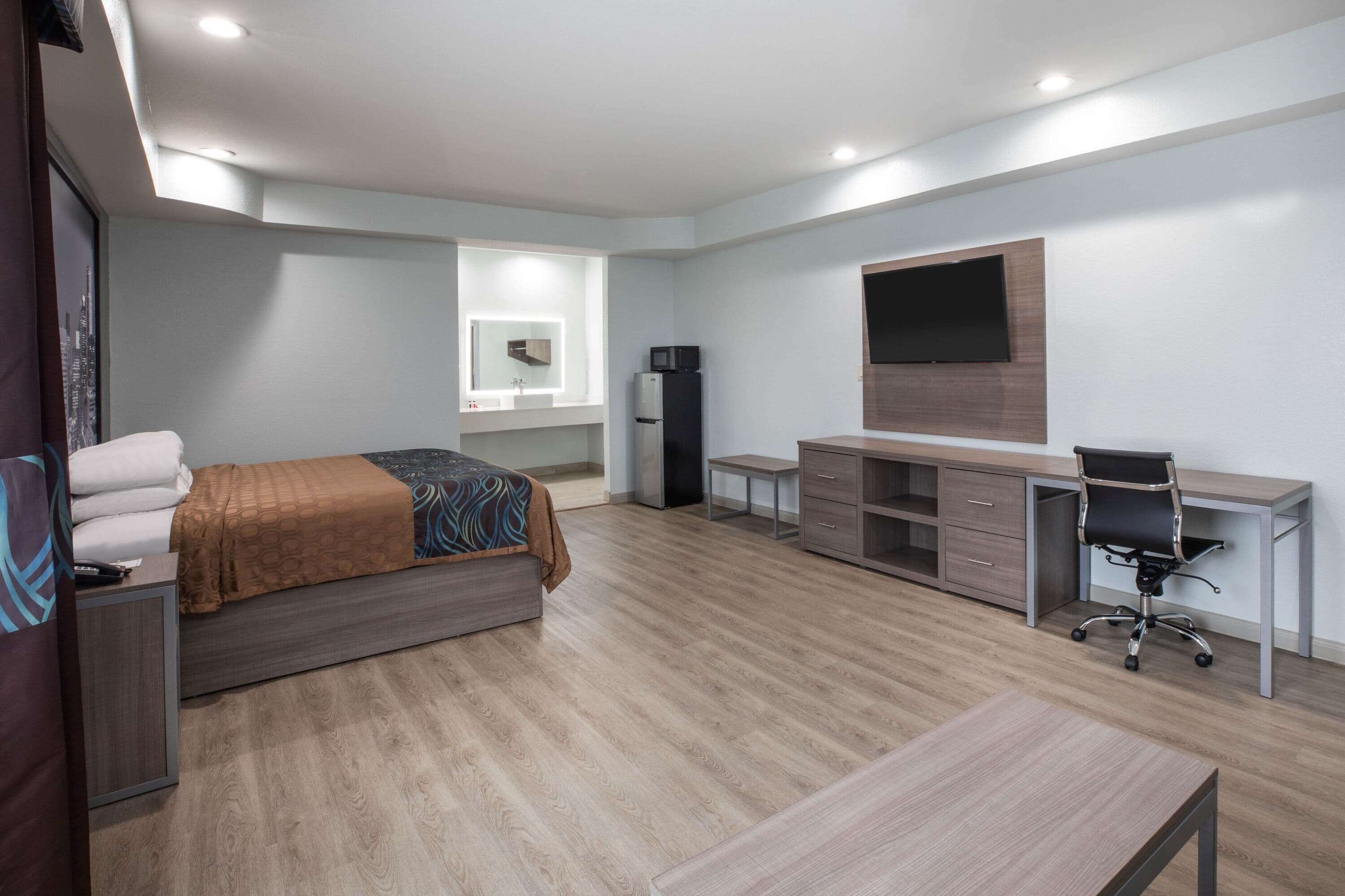 A modern hotel room with a bed, desk, chair, and a flat-screen TV mounted on the wall.