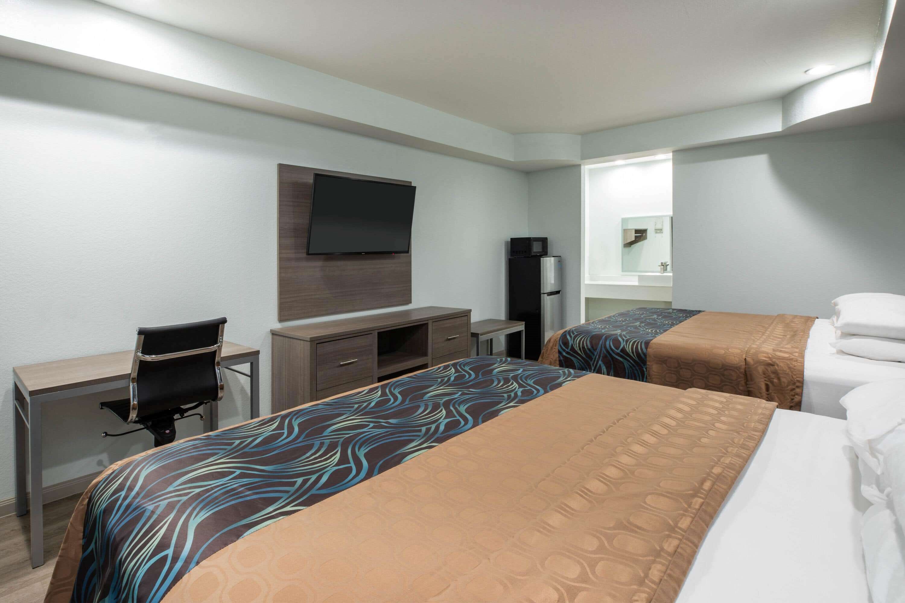 A hotel room with two beds, a desk, a chair, a television, and a refrigerator.