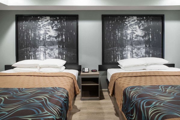 Ein Hotelzimmer mit zwei Betten, jeweils mit einem gemusterten Bettbezug, einem Nachttisch mit Telefon und einer Uhr sowie zwei großen gerahmten Bildern einer Waldszene an der Wand.