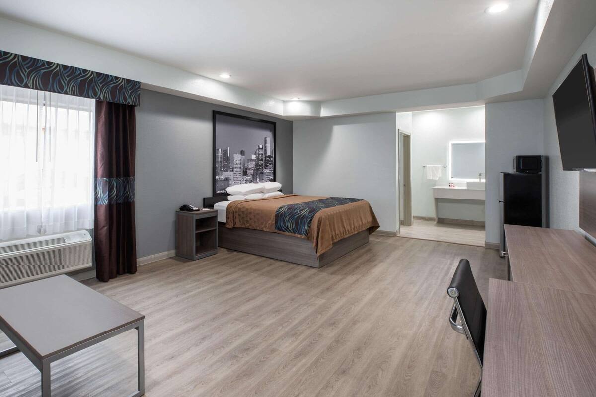 Habitación de hotel con cama, mesita de noche, escritorio, televisor de pantalla plana y baño visible a través de una puerta abierta.
