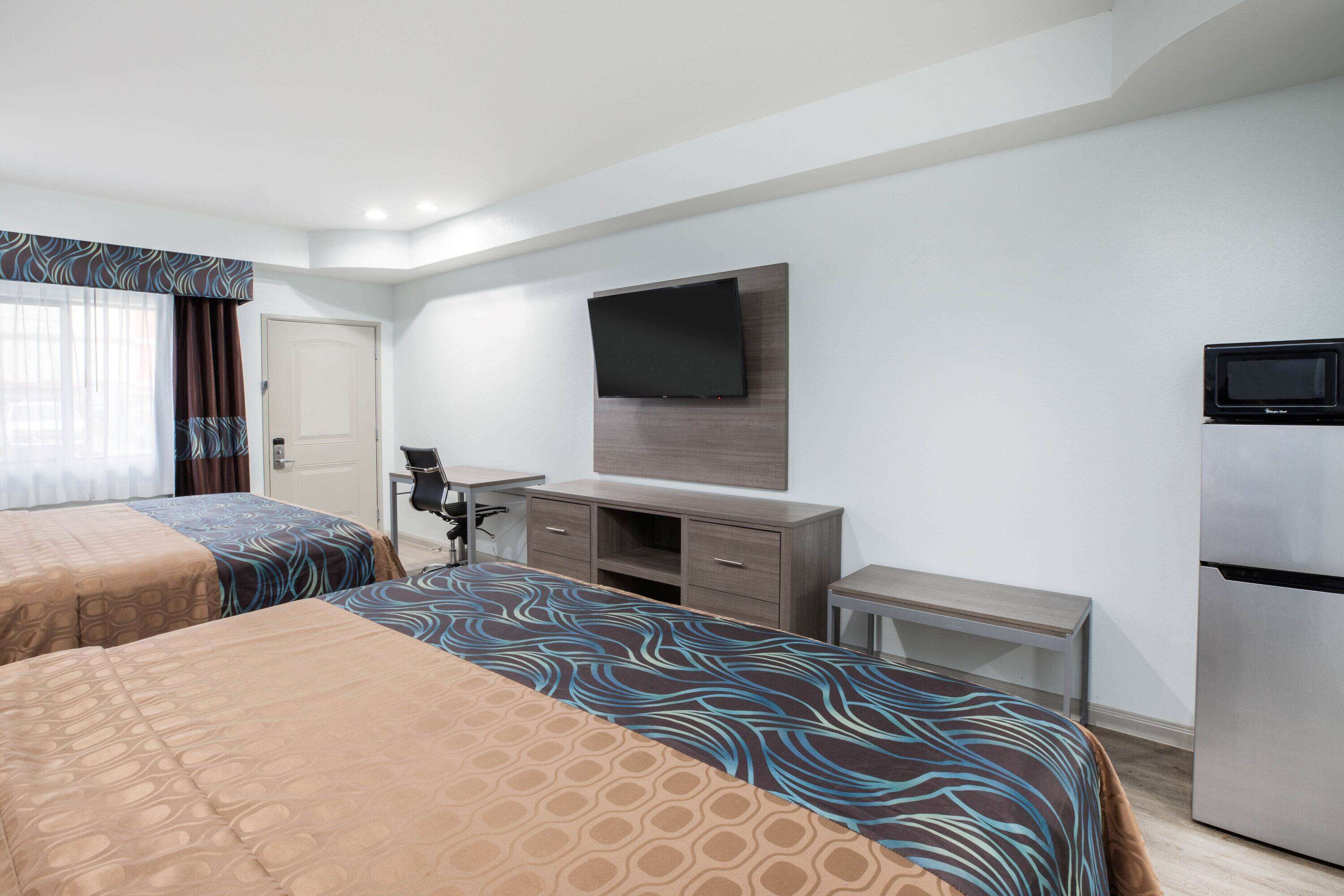 Une chambre d’hôtel avec deux lits, un bureau, un téléviseur à écran plat et un réfrigérateur.