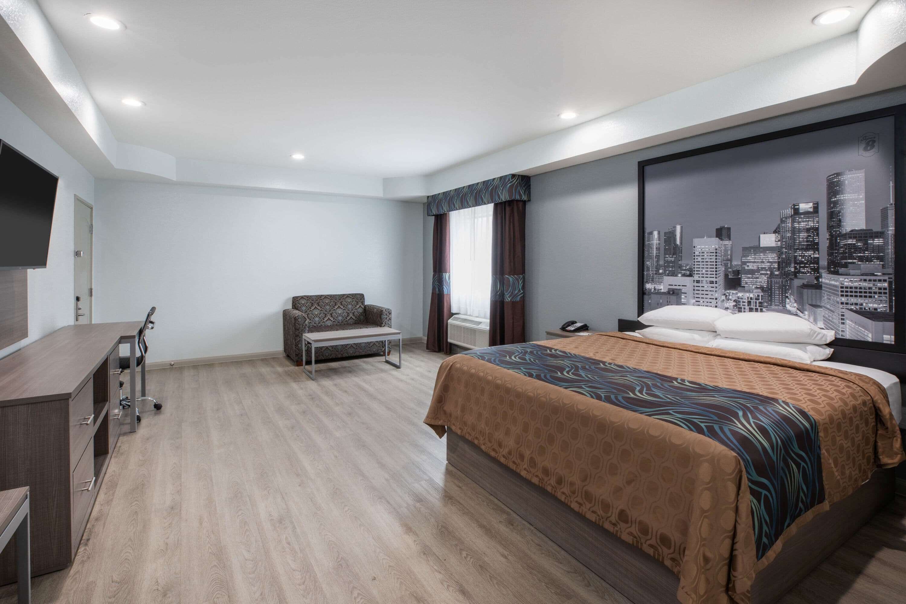 Un hotel moderno con una cama grande, un escritorio, una silla y un cuadro de un paisaje urbano en la pared.
