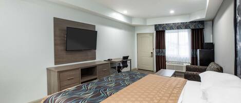 A hotel room with a bed, a desk, a chair, a television, and a door.