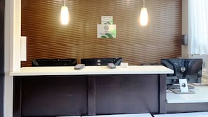 A reception desk with a wooden wall, two pendant lights, a sign indicating a non-smoking facility, and a computer setup on the right. - Wingate by Wyndham JFK Airport/Far Rockaway (Far Rockaway)